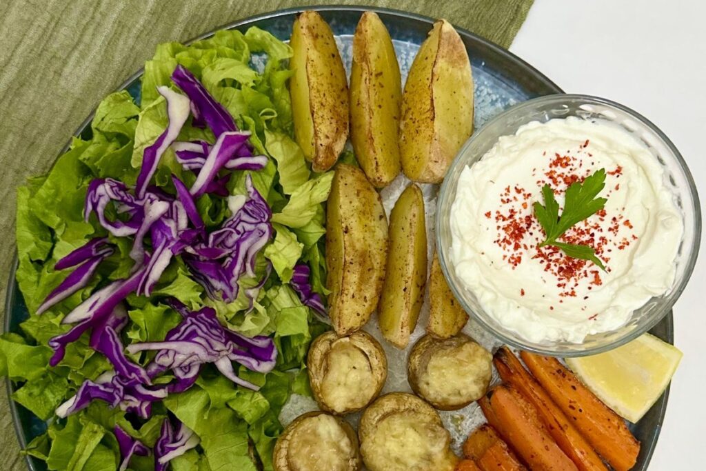 Prato saudável e colorido visto de cima, com folhas verdes, repolho roxo, batatas, cogumelos, cenoura e molho