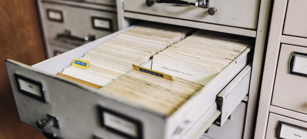 Gaveta de arquivo antigo aberta, repleta de fichas e documentos organizados, representando o arquivamento de documentos ao final de um contrato de terceirização.