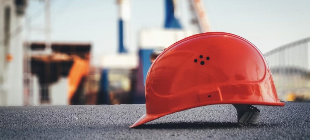Capacete de segurança laranja no chão de canteiro de obras, representando equipamento de proteção individual