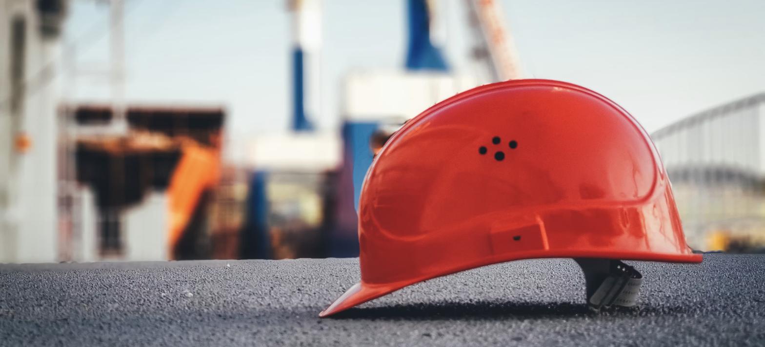 Capacete de segurança laranja no chão de canteiro de obras, representando equipamento de proteção individual