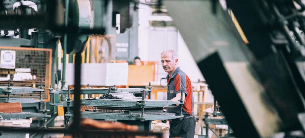 Trabalhador em chão de fábrica operando maquinário industrial pesado, cercado de equipamentos metálicos, representando o ambiente típico onde ocorre uma fiscalização do trabalho em terceirizados.