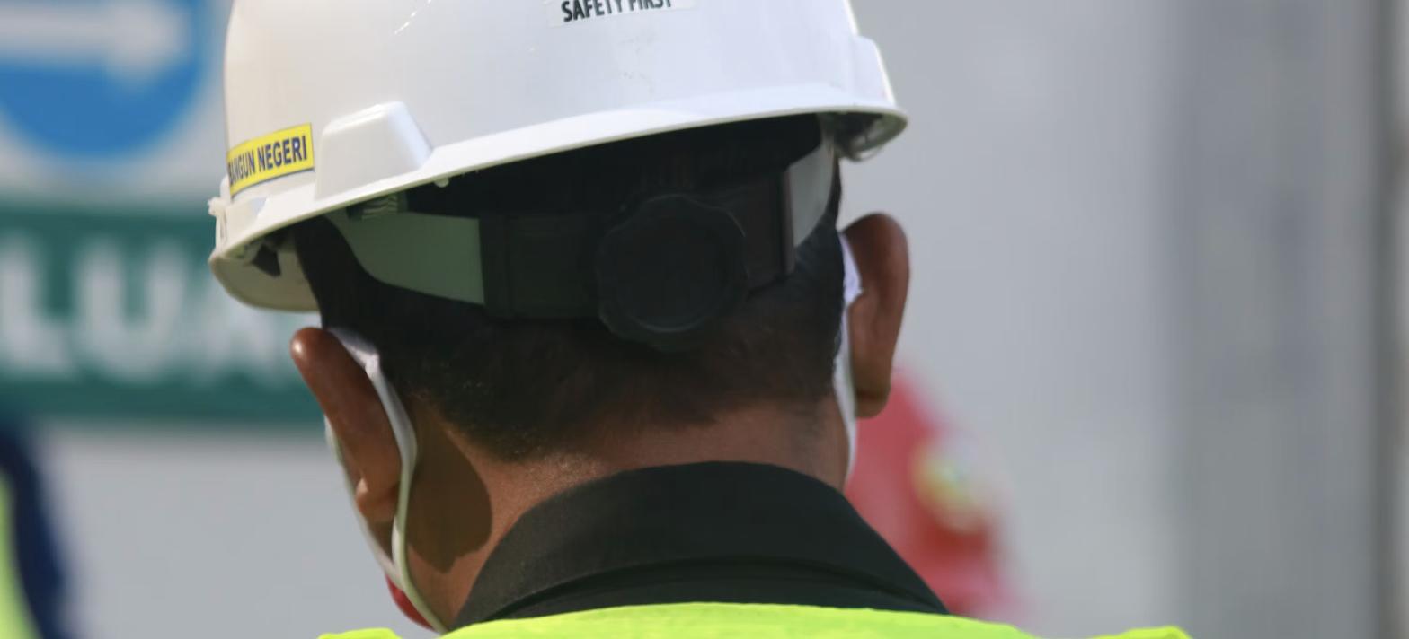 Trabalhador de campo com capacete e colete de segurança em planta industrial, representando a Ordem de Serviço de SST