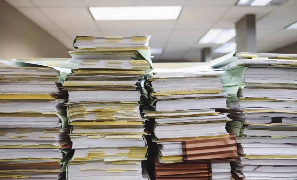 Pilhas de pastas e documentos arquivados em escritório, representando registros de exames ocupacionais
